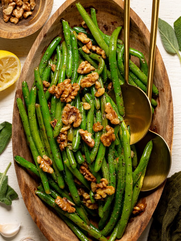 Green beans in a wooden serving platter with two gold spoons.
