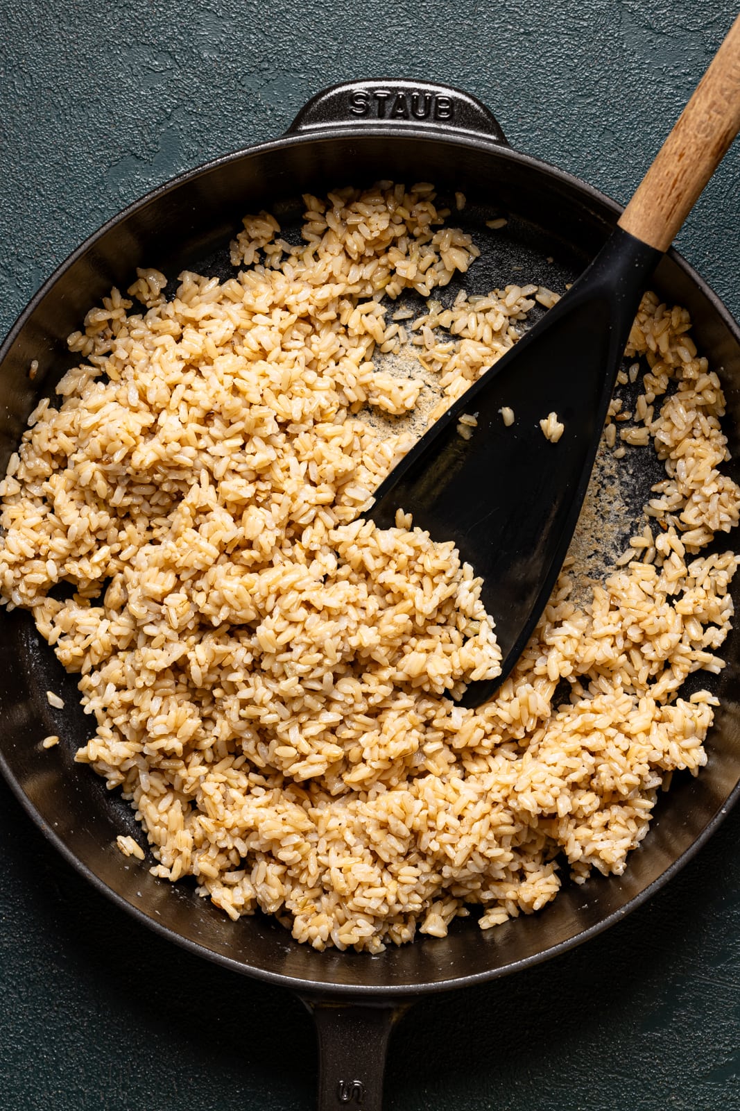 Cooked brown rice in a black skillet with a spoon.