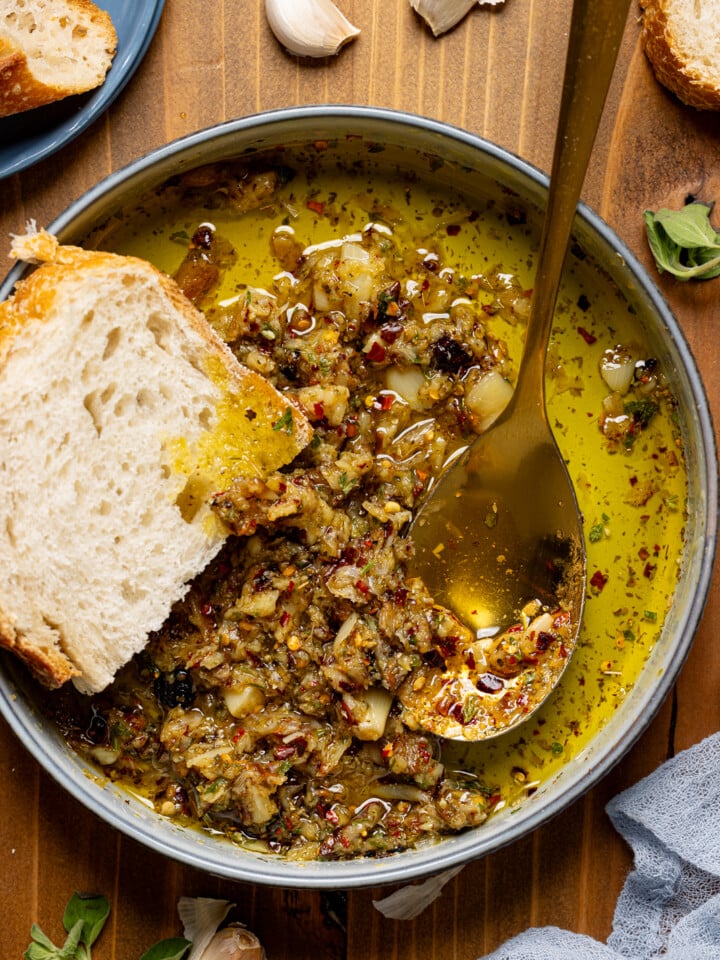 Up close shot of garlic dip in a bowl with a spoon and piece of bread.