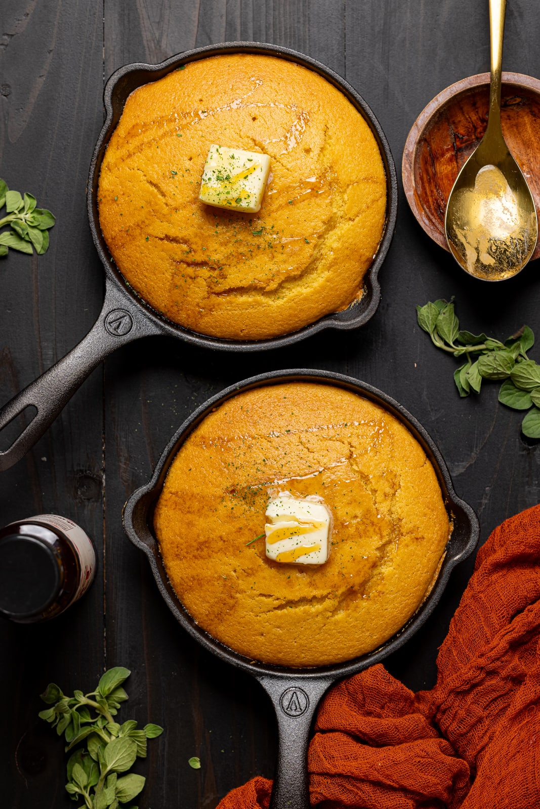 Two hot honey cornbreads in skillets with a slice of butter and hot honey drizzle.