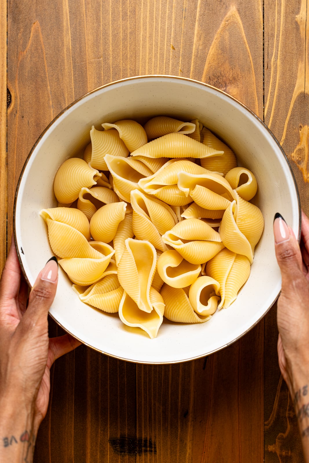 Cooked pasta shells in a white bowl being held.