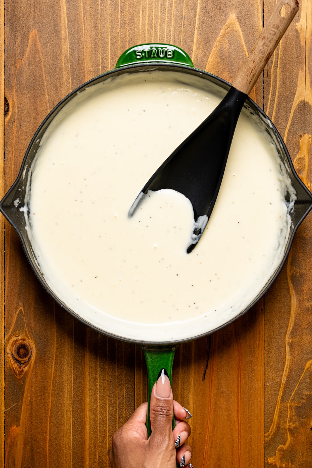 White mac and cheese sauce in a black skillet and a black spoon.