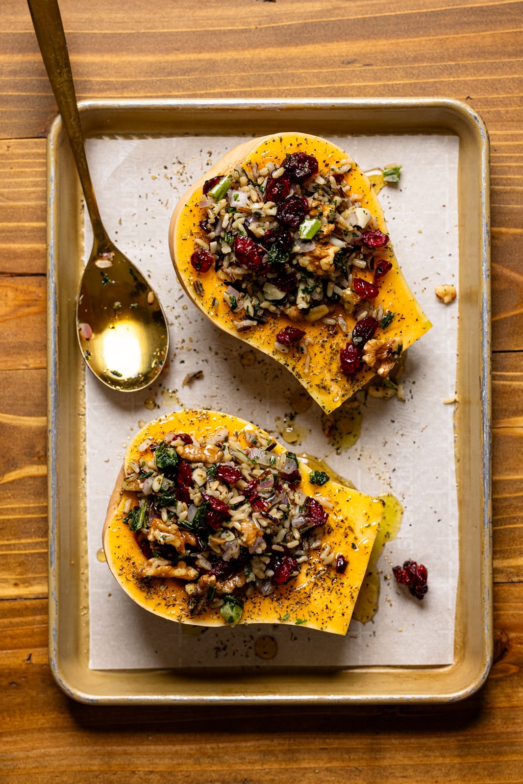Stuffed butternut squash on a baking sheet with parchment paper and a spoon.