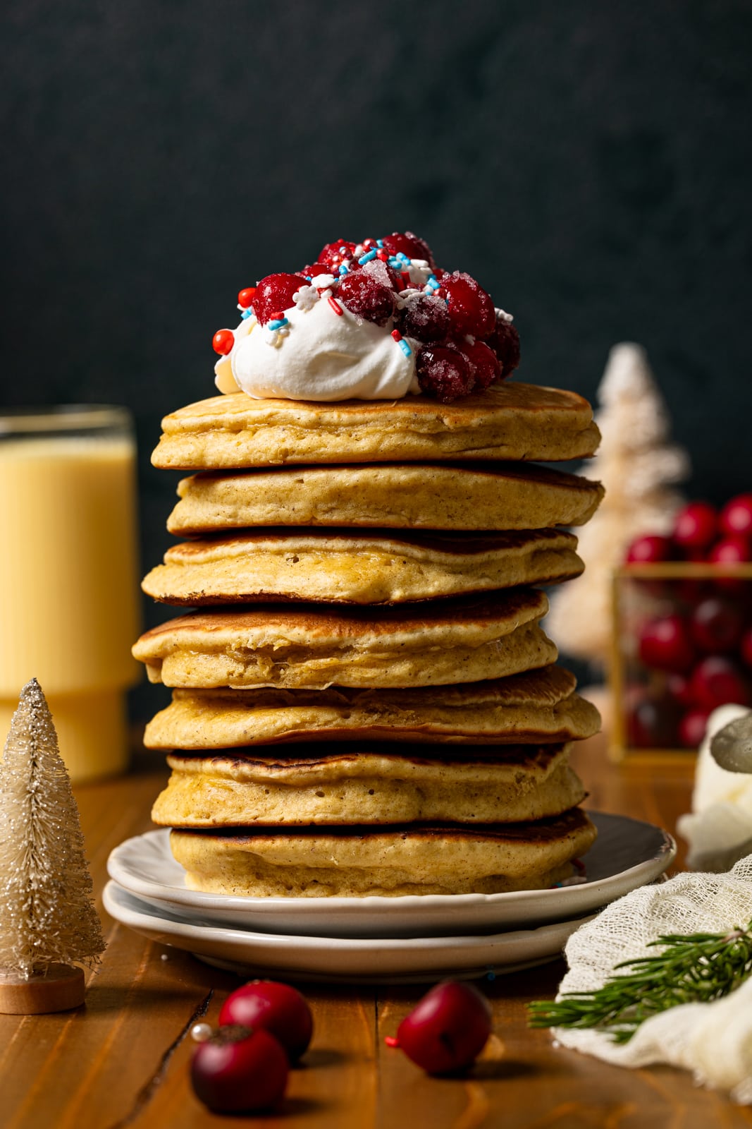 Stack of pancakes on two white plates with glass of eggnog in the background.