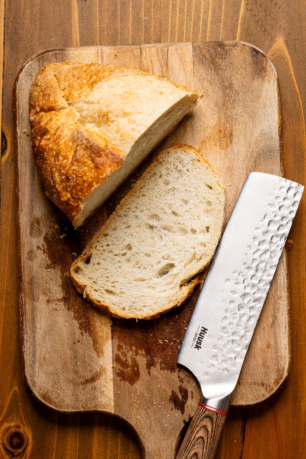 Loaf of bread sliced on a cutting board with a knife. 