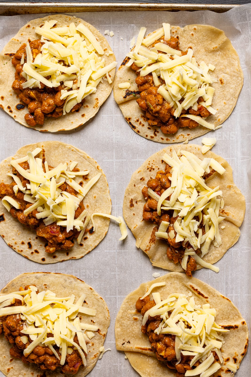 Tacos assembled on a baking sheet with parchment paper.