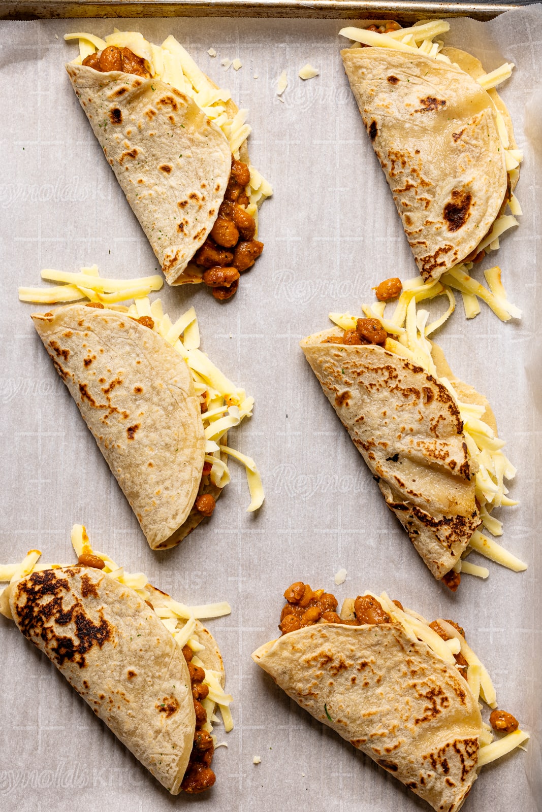 BBQ pinto bean tacos folded on baking sheet with parchment paper.