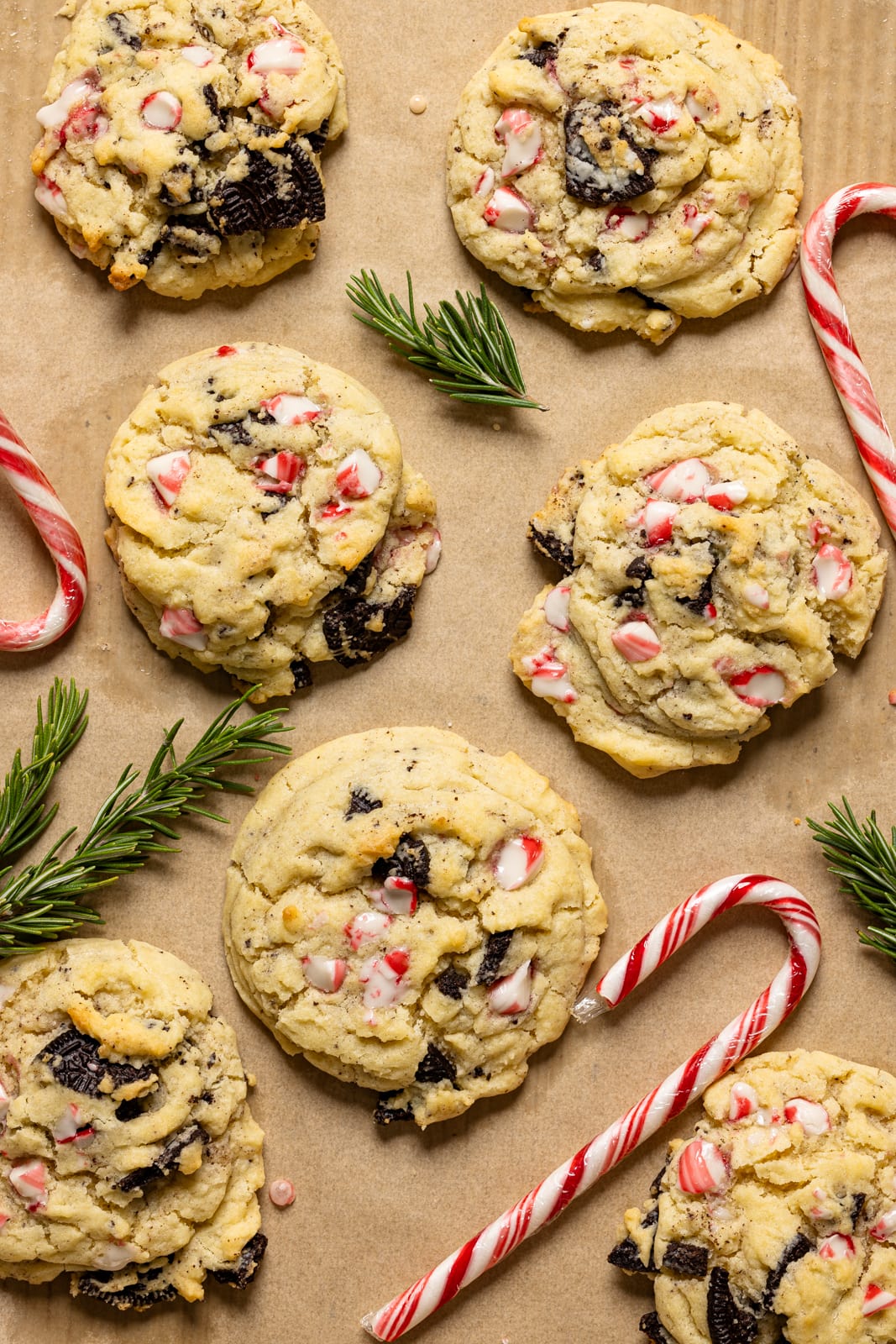 Baked cookies on a baking sheet with parchment paper with candy canes and rosemary.