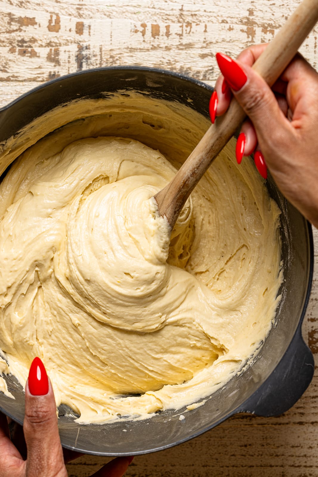 Bowl with cake batter being stirred with wooden spoon.