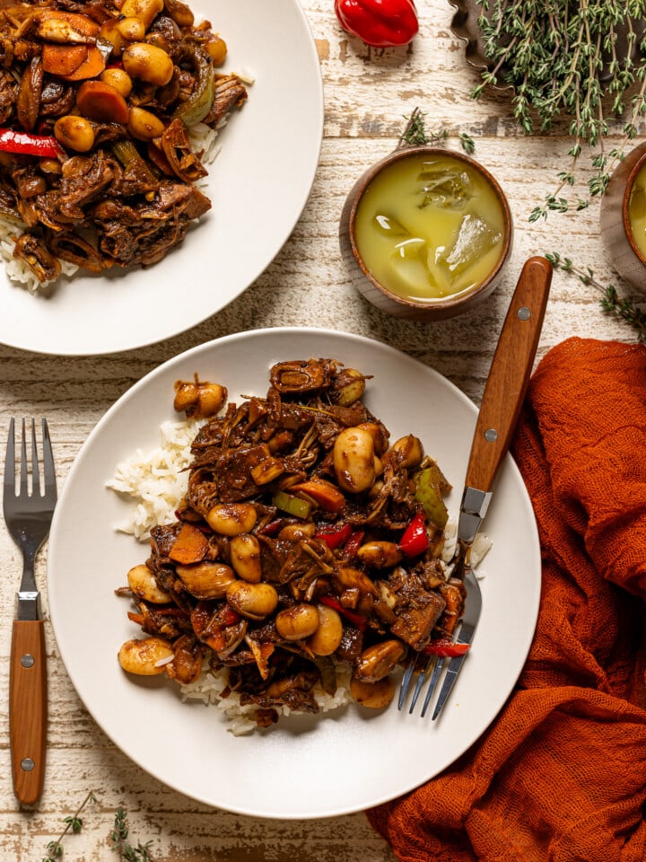 Two plates of plant-based oxtail with forks and drinks.