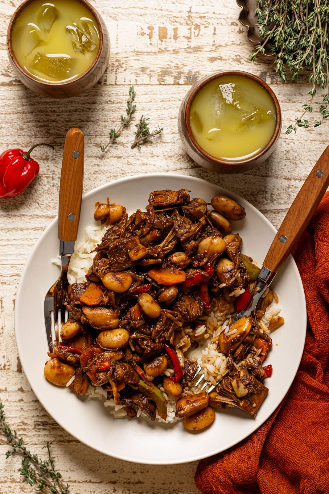 Plate full of plant-based oxtail with two forks and two cups of drinks.