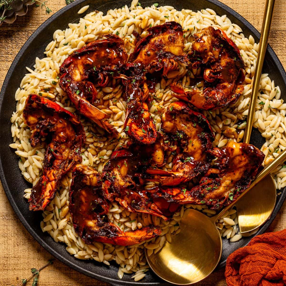 Up close shot of lobster and orzo in a skillet with serving spoons.