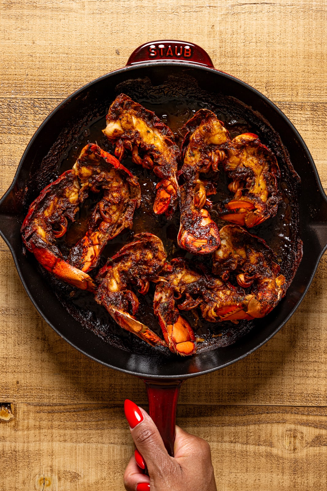 BBQ jerk lobster tails in a skillet being held.