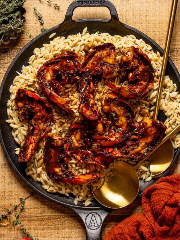 Up close shot of lobster and orzo in a skillet with serving spoons.