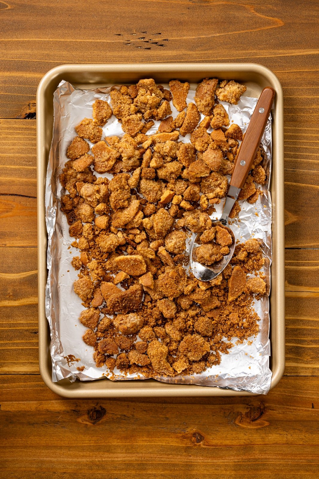 Cookie crumble topping on a baking sheet with a spoon.