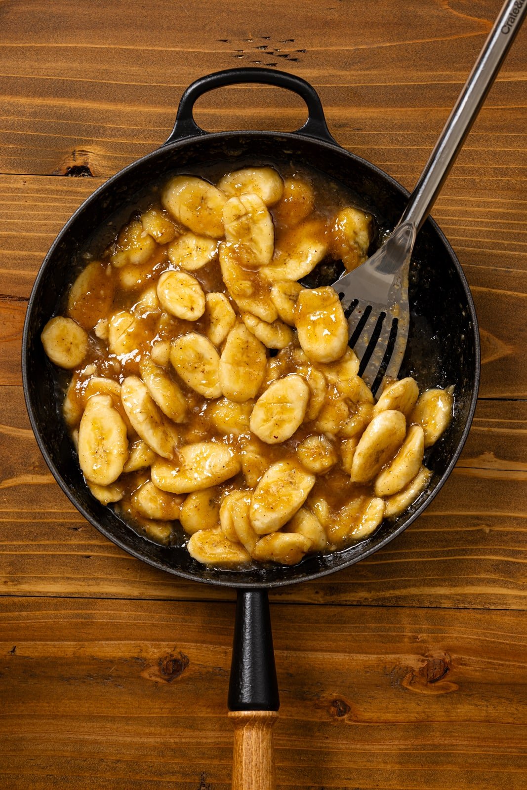 Caramelized bananas in a black skillet with a spatula. 