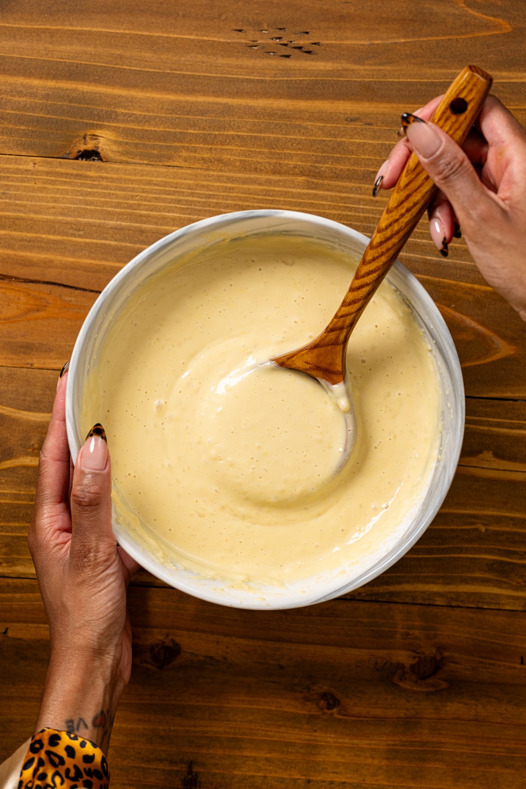 Homemade vanilla pudding a bowl being stirred with a wooden spoon.