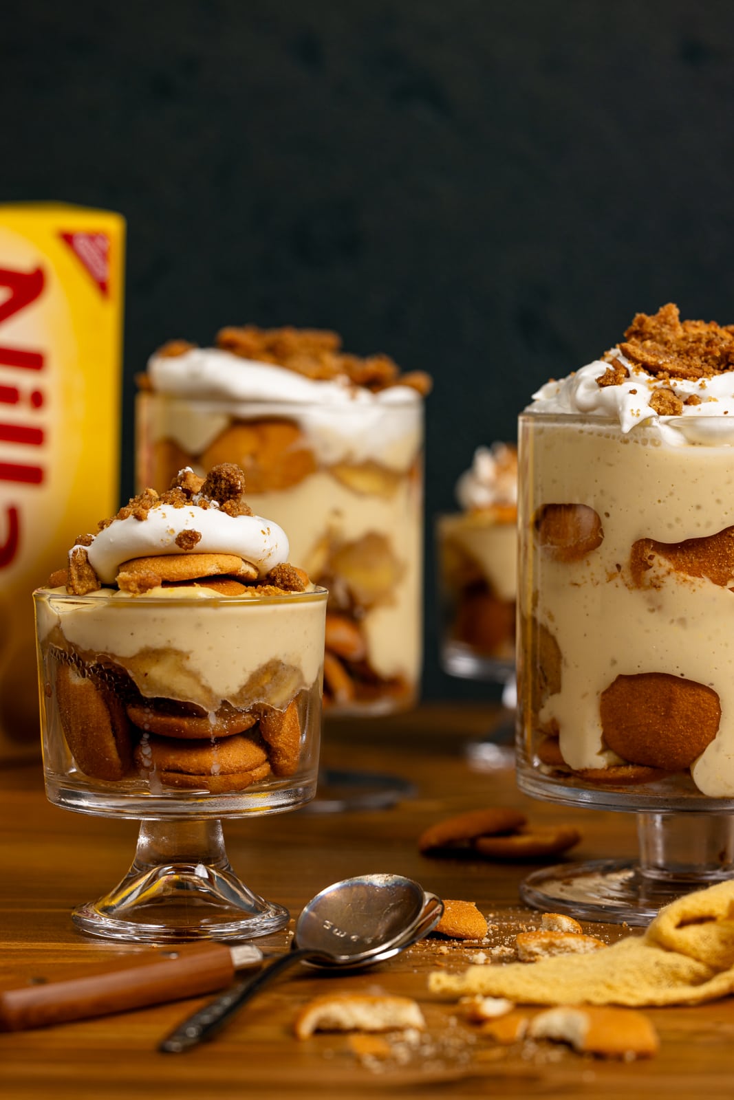 Banana pudding in trifle bowls with a box of vanilla wafers and spoons.