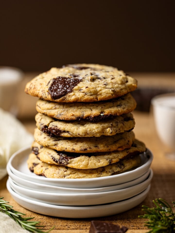 Up close shot of stack of cookies on white plates with a glass of milk in the background.