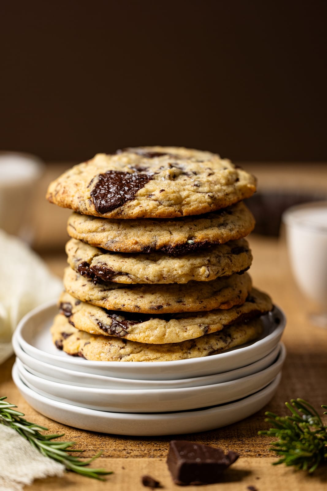 Up close shot of stack of cookies on white plates with a glass of milk in the background.