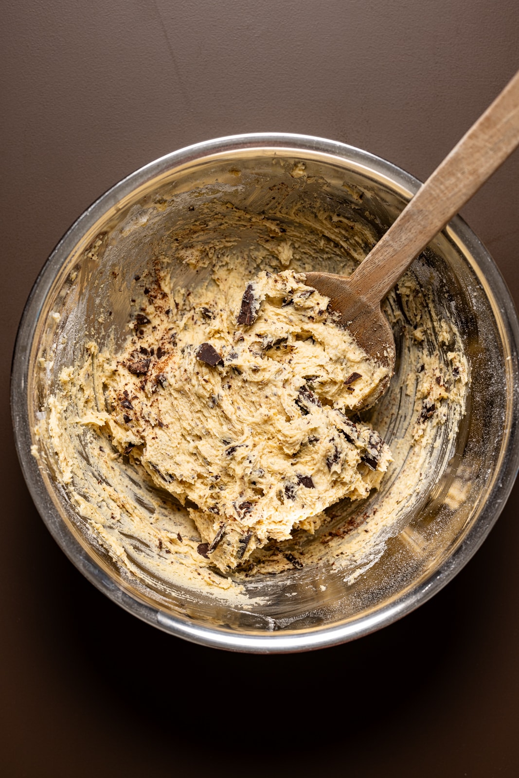 Cookie batter in a silver bowl with a wooden spoon.