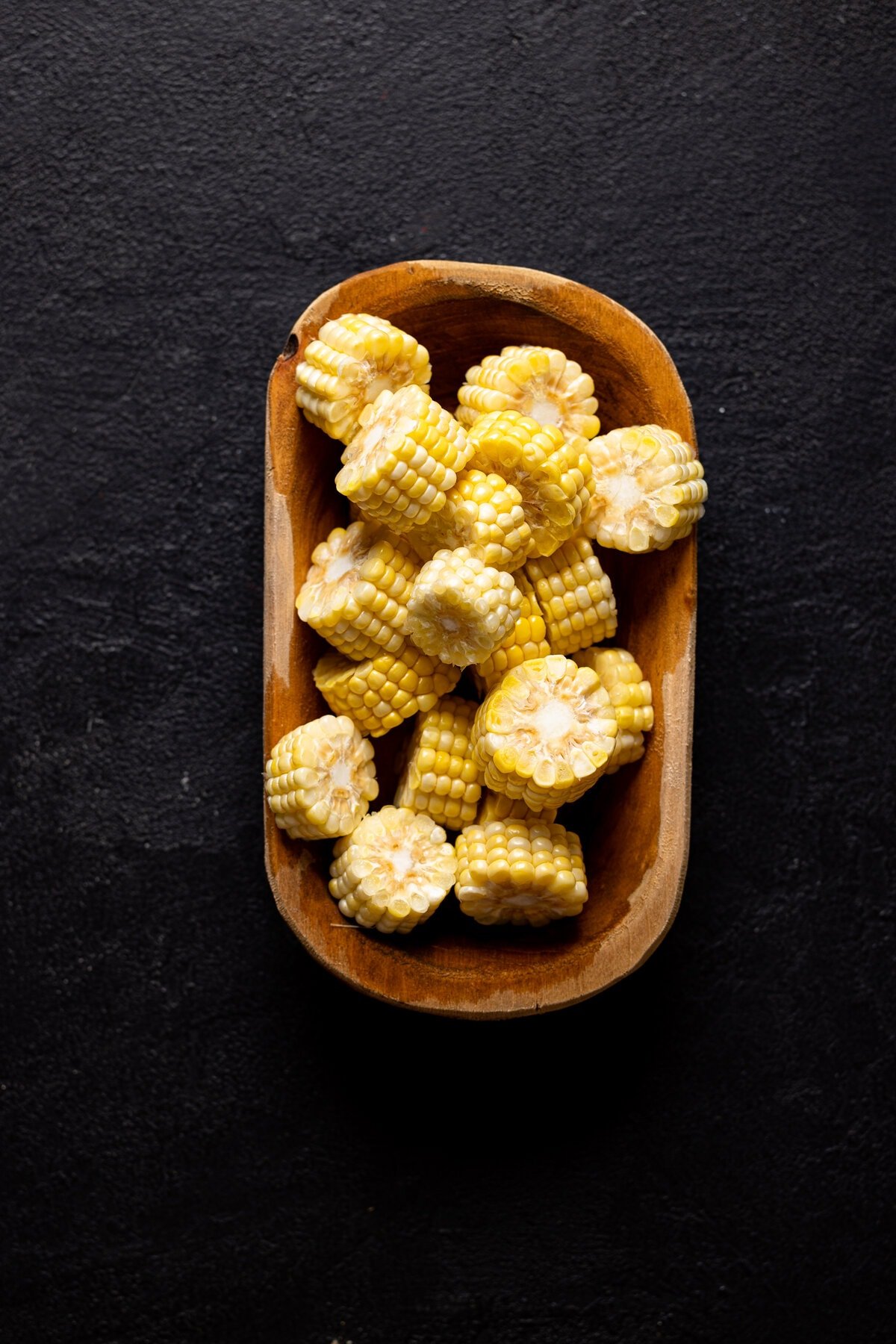 Chopped corn in a brown bowl on a black table.