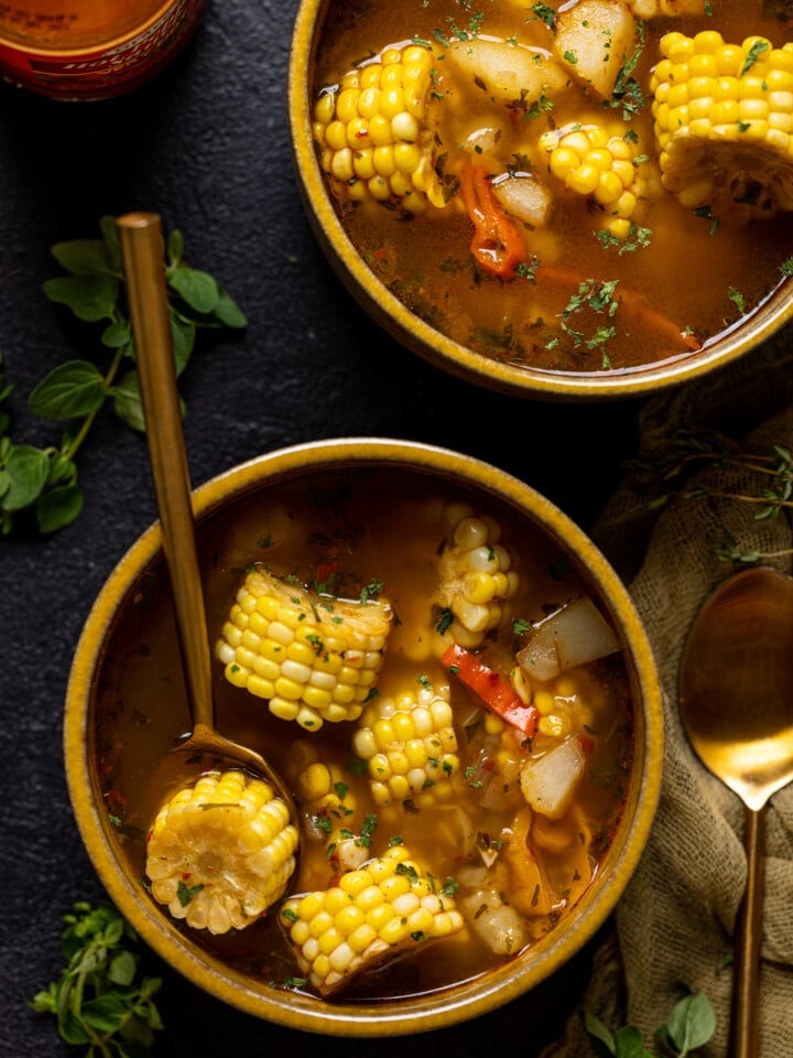 Up close shot of bowls of corn soup with a spoon and pepper sauce.