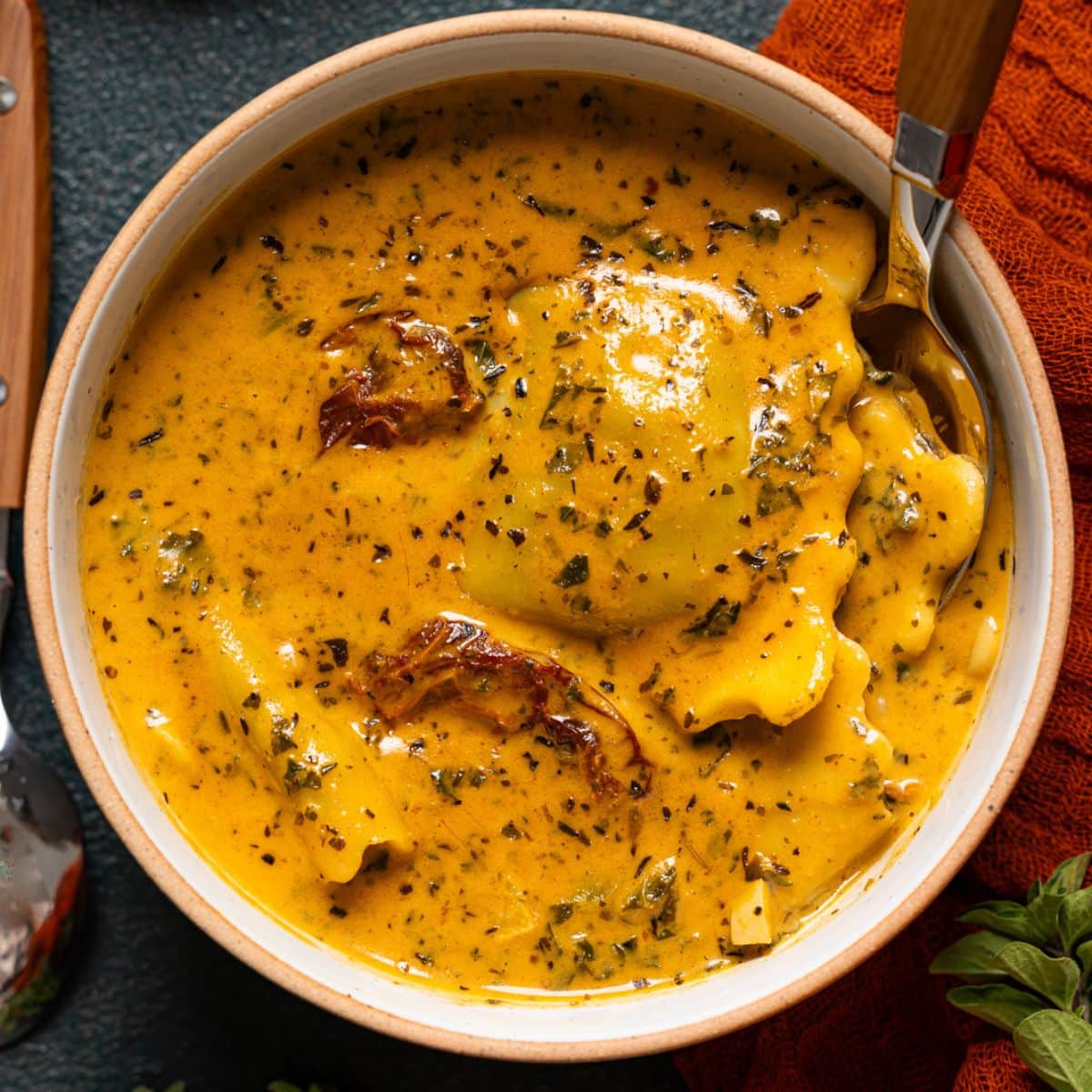 Up close shot of ravioli soup with a spoon and herbs.