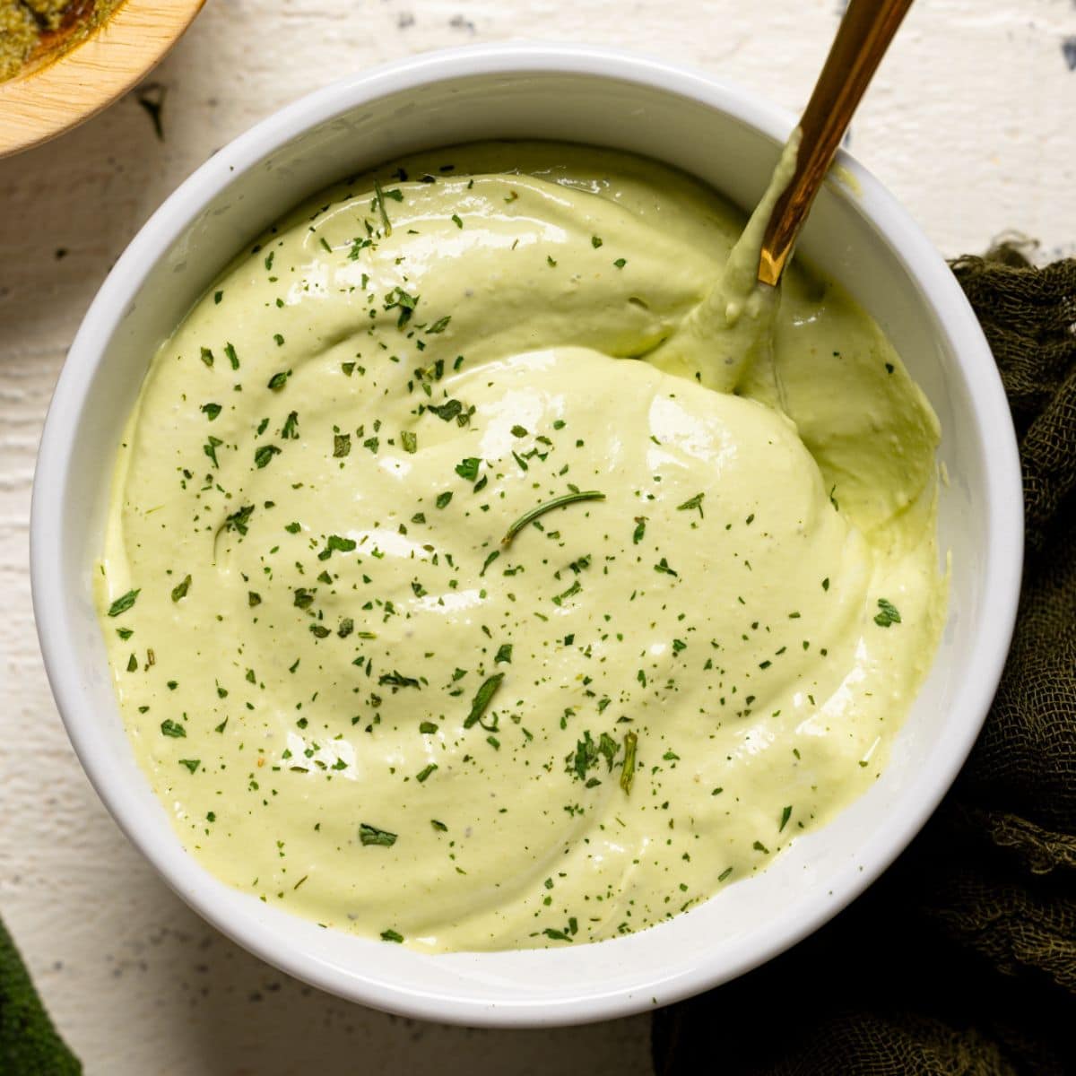 Up close shot of mayo in a white bowl with a gold spoon.