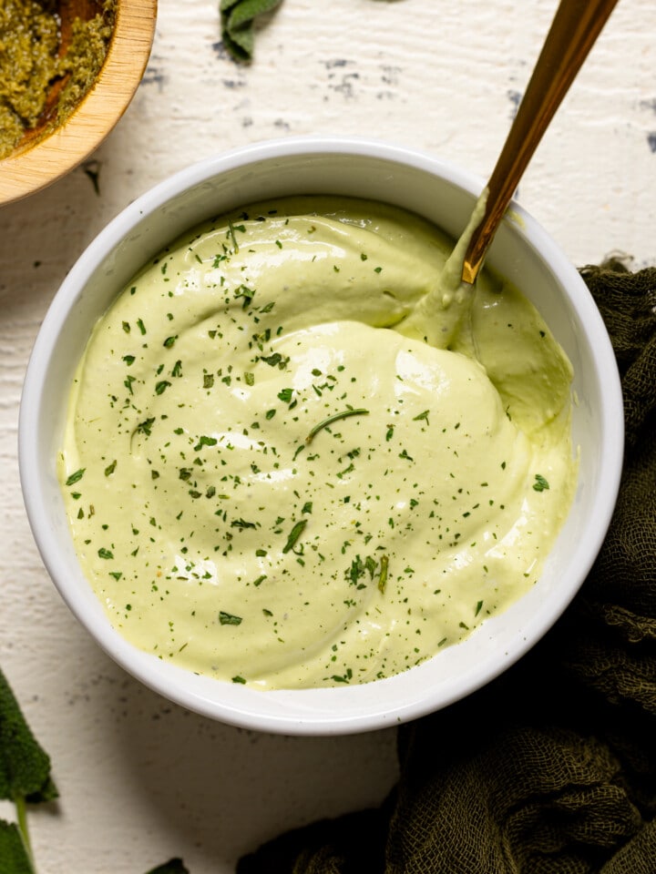 Up close shot of mayo in a white bowl with a gold spoon.