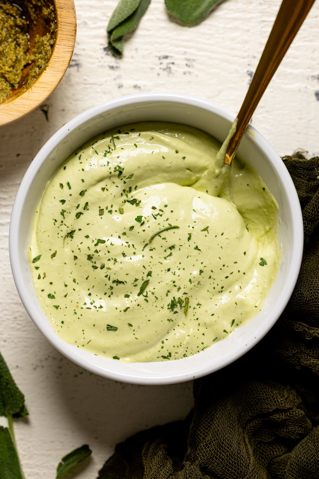 Up close shot of mayo in a white bowl with a gold spoon.