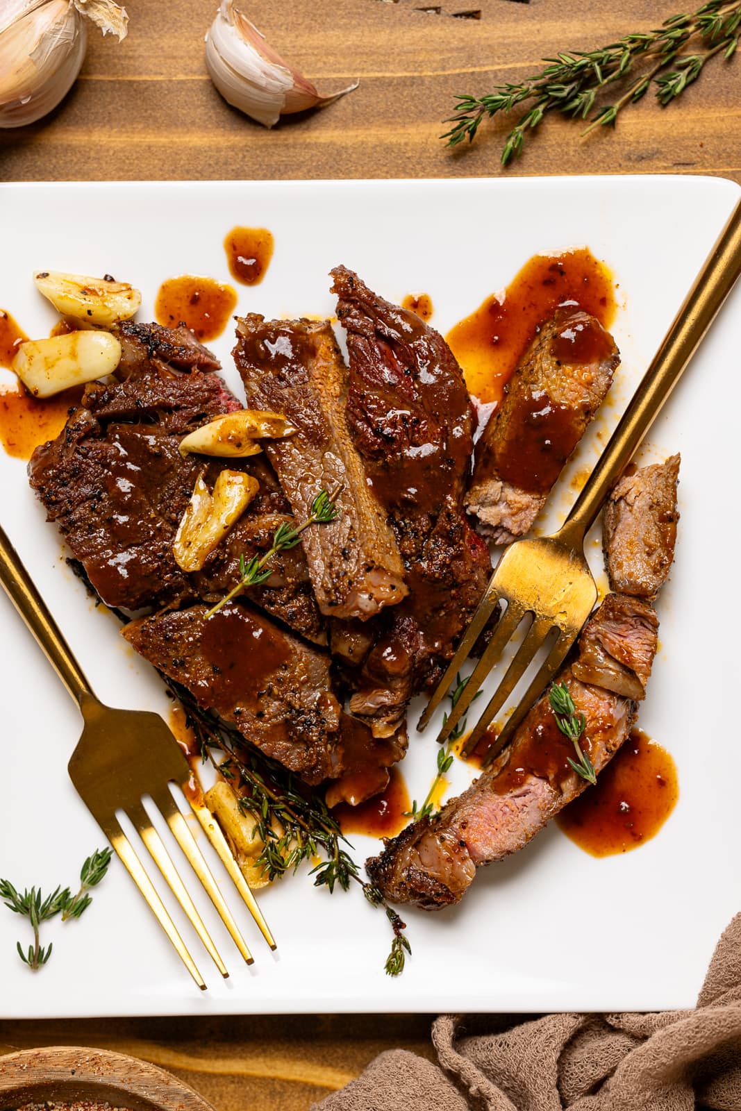 Sliced steak on a white plate with sauce and two forks.