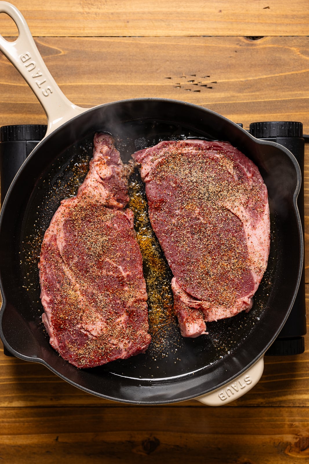Steak fillets in a skillet over a stove top.