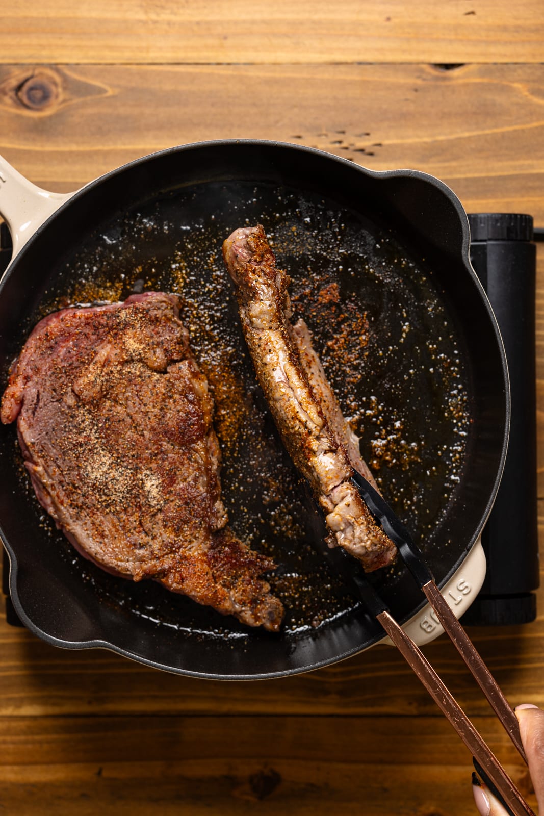 Steak being held with a tong on it's side while searing.