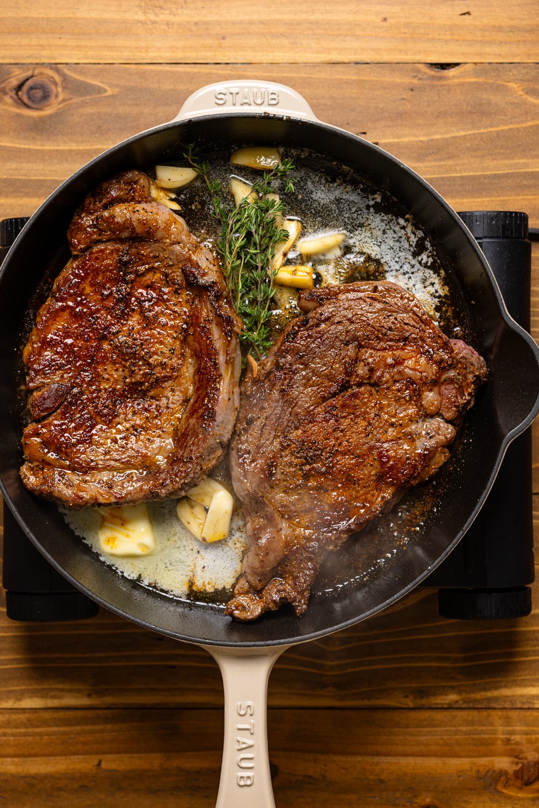 Steak being seared with garlic cloves + rosemary.