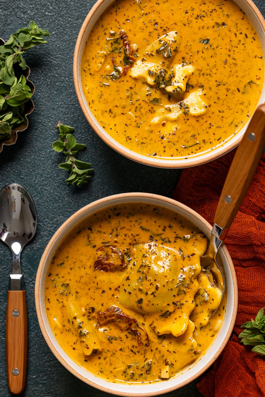 Two bowls of ravioli soup with spoons. 