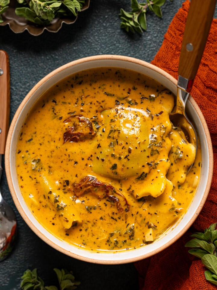 Up close shot of ravioli soup with a spoon and herbs.