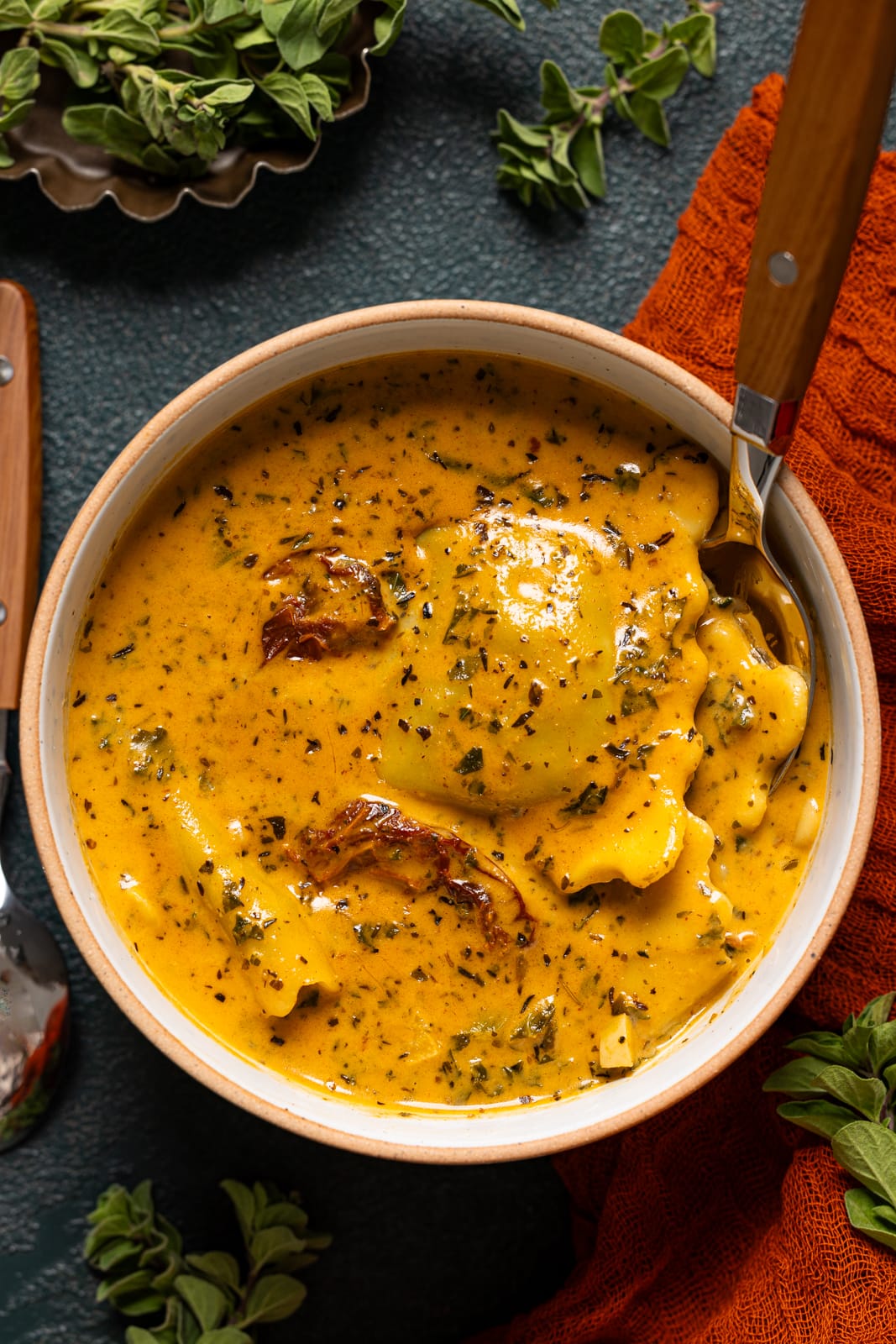 Up close shot of ravioli soup with a spoon and herbs.