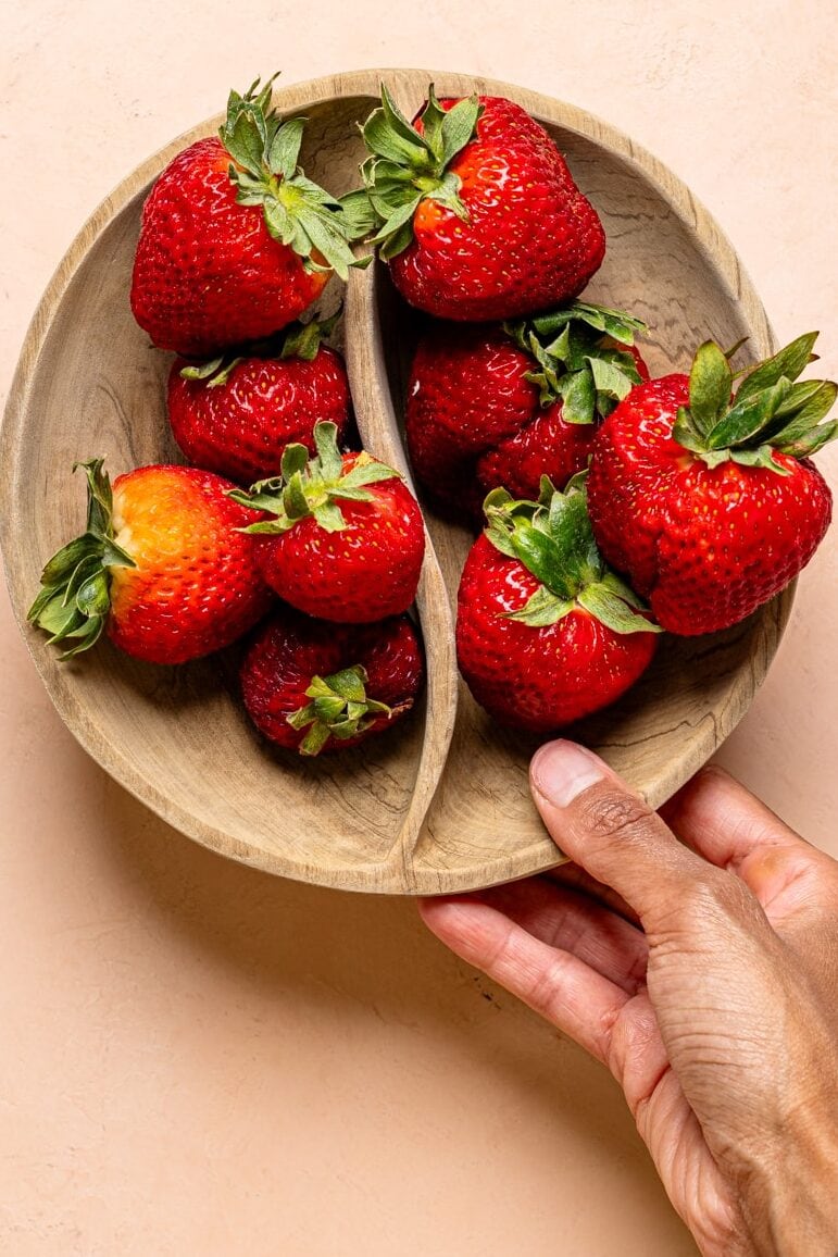 Fresh strawberries in a brown bowl on a peach table.