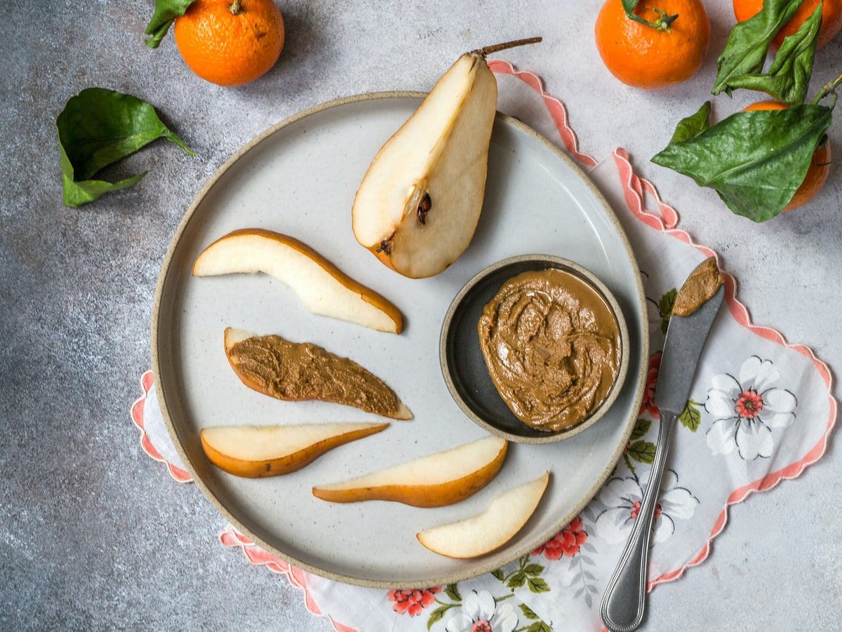 Pear cut up with nut butter on gray plate.
