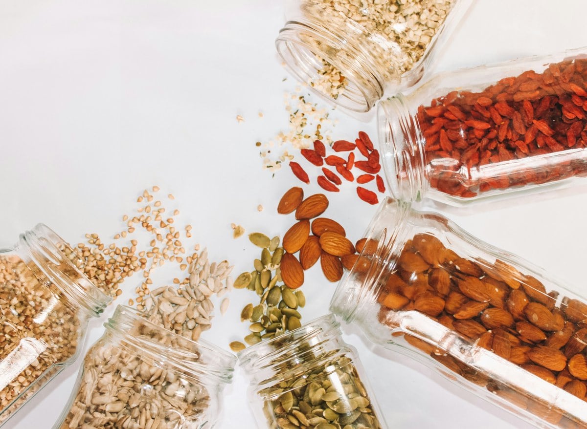 Nuts and seeds in jars on white counter.