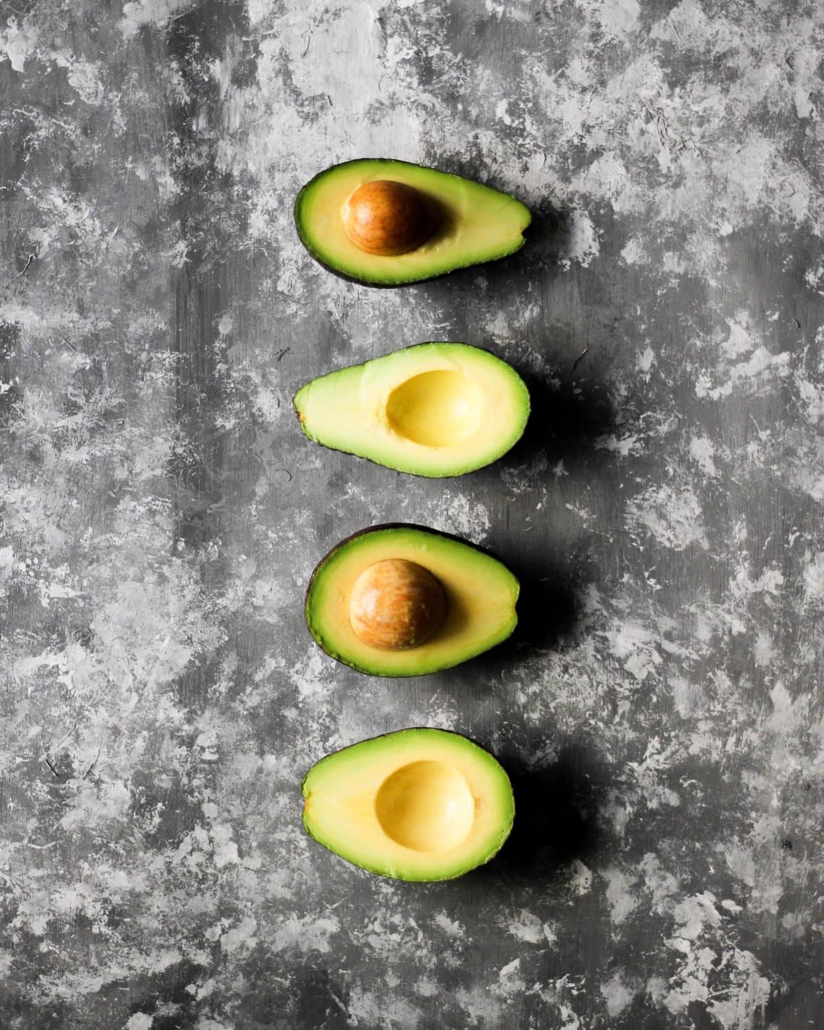 Fresh produce of avocados cut in half on a grey countertop. 