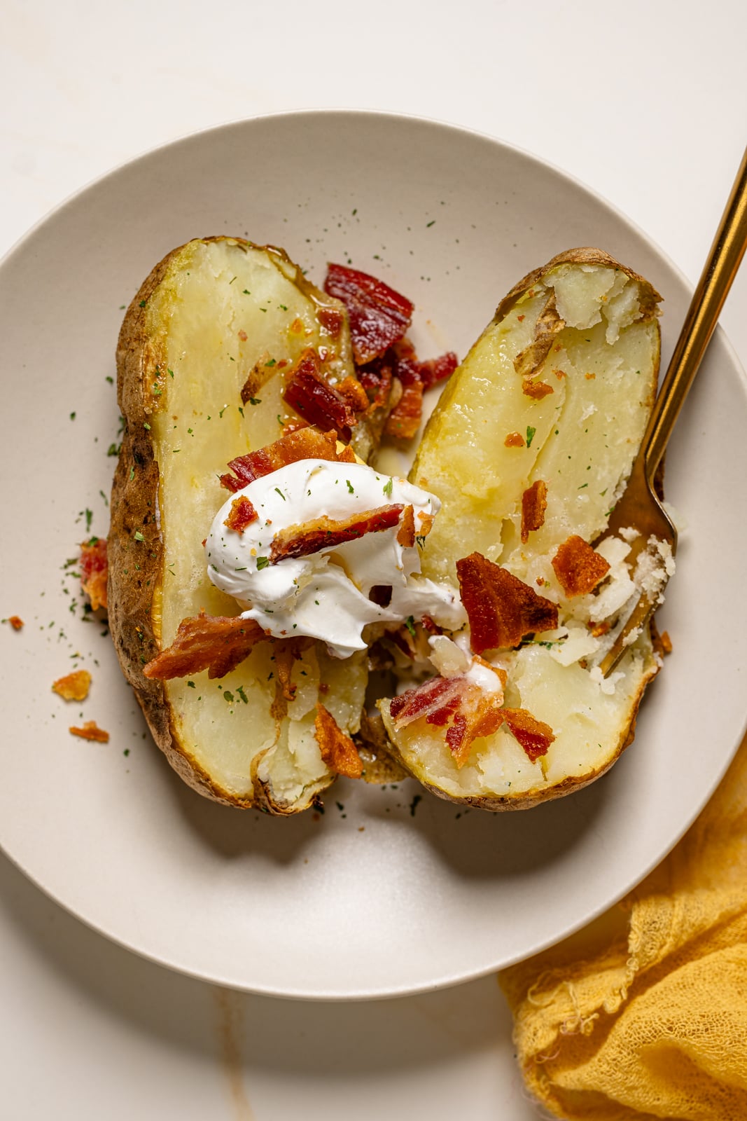 Opened baked potato on a plate with bacon and sour cream with a fork.