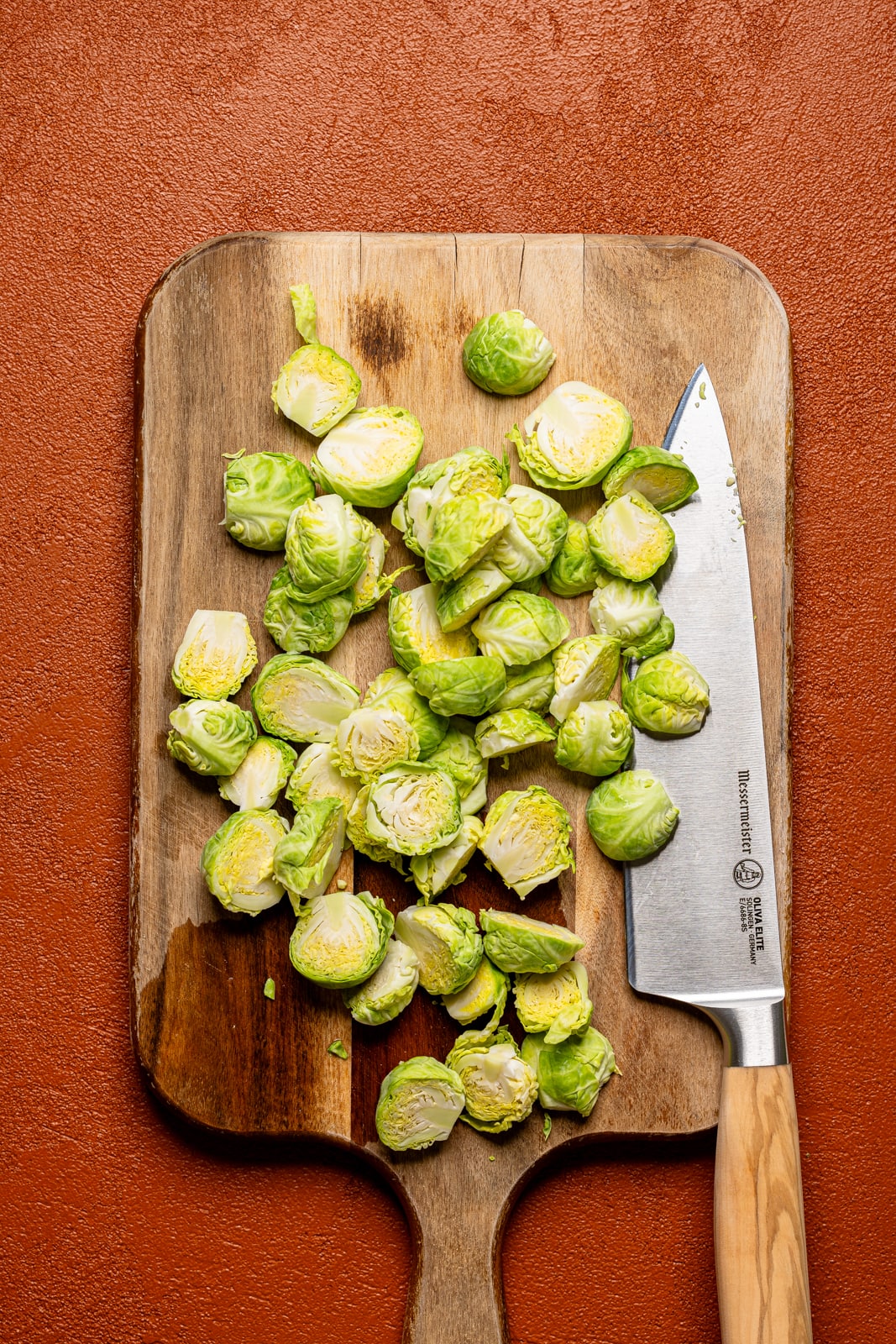 Brussels sprouts chopped on a cutting board with a knife.