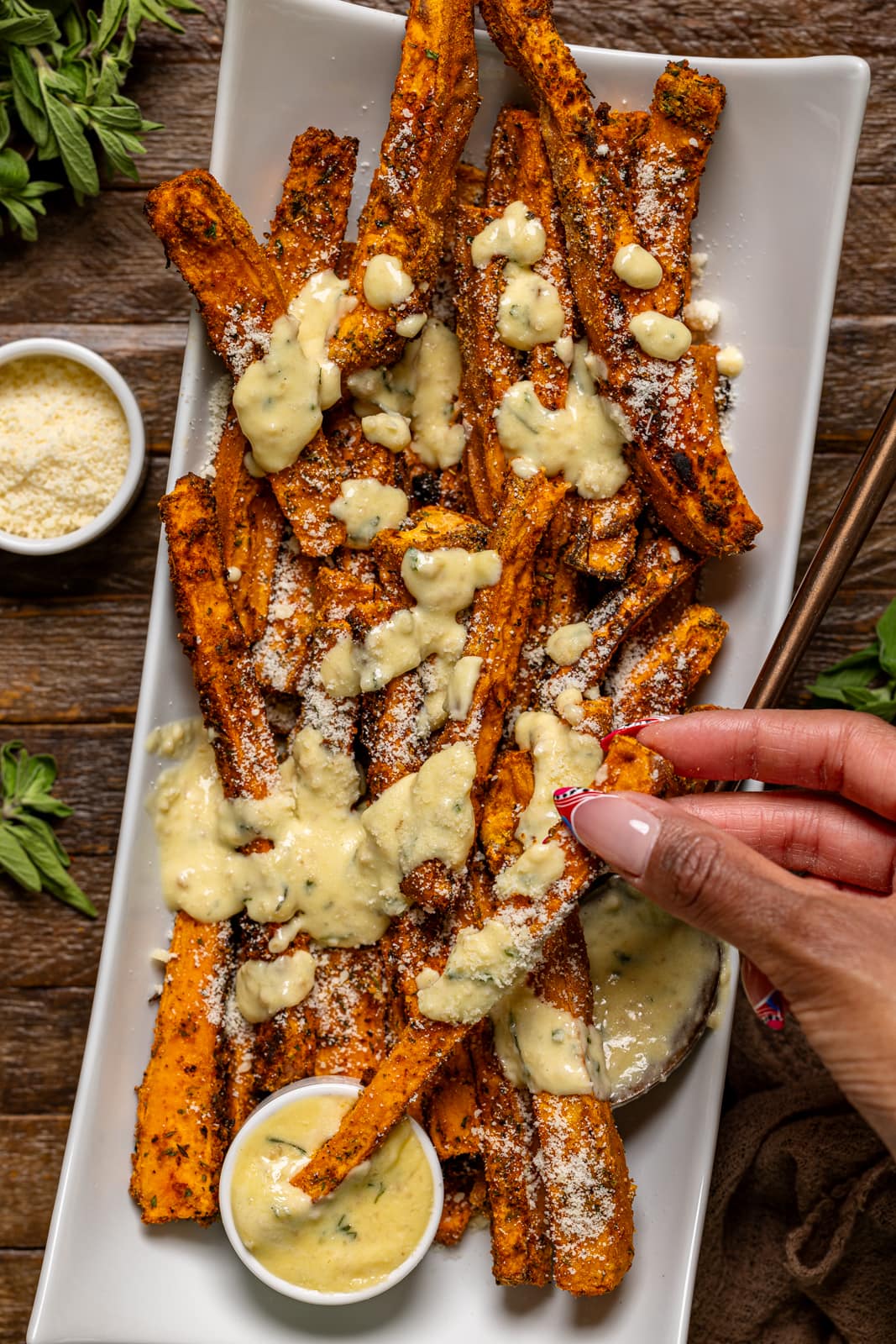 Fries on a white platter with sauce being held.