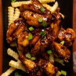 Wings served on top of fries on a black platter.