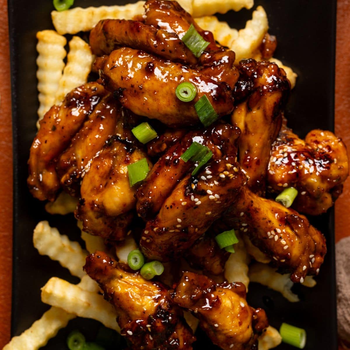 Wings served on top of fries on a black platter.