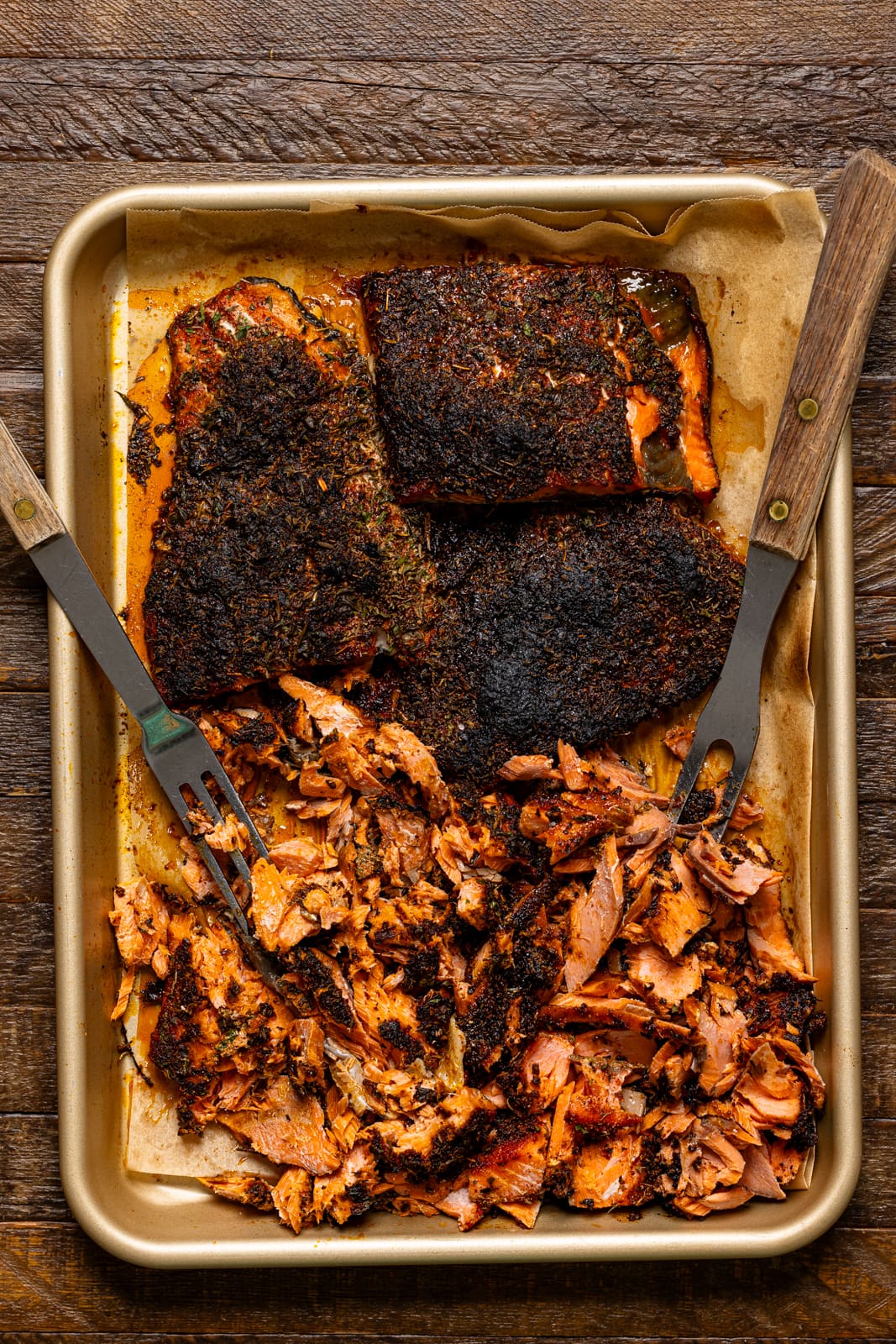 Blackened salmon baked on a baking sheet with two forks.