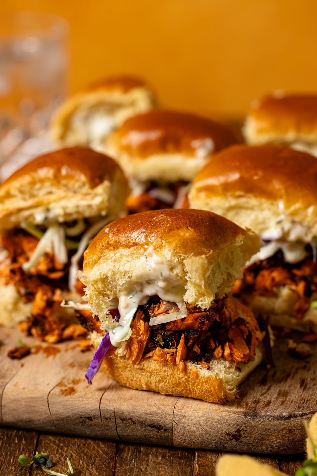 Sliders on a brown wood board with a drink in background.