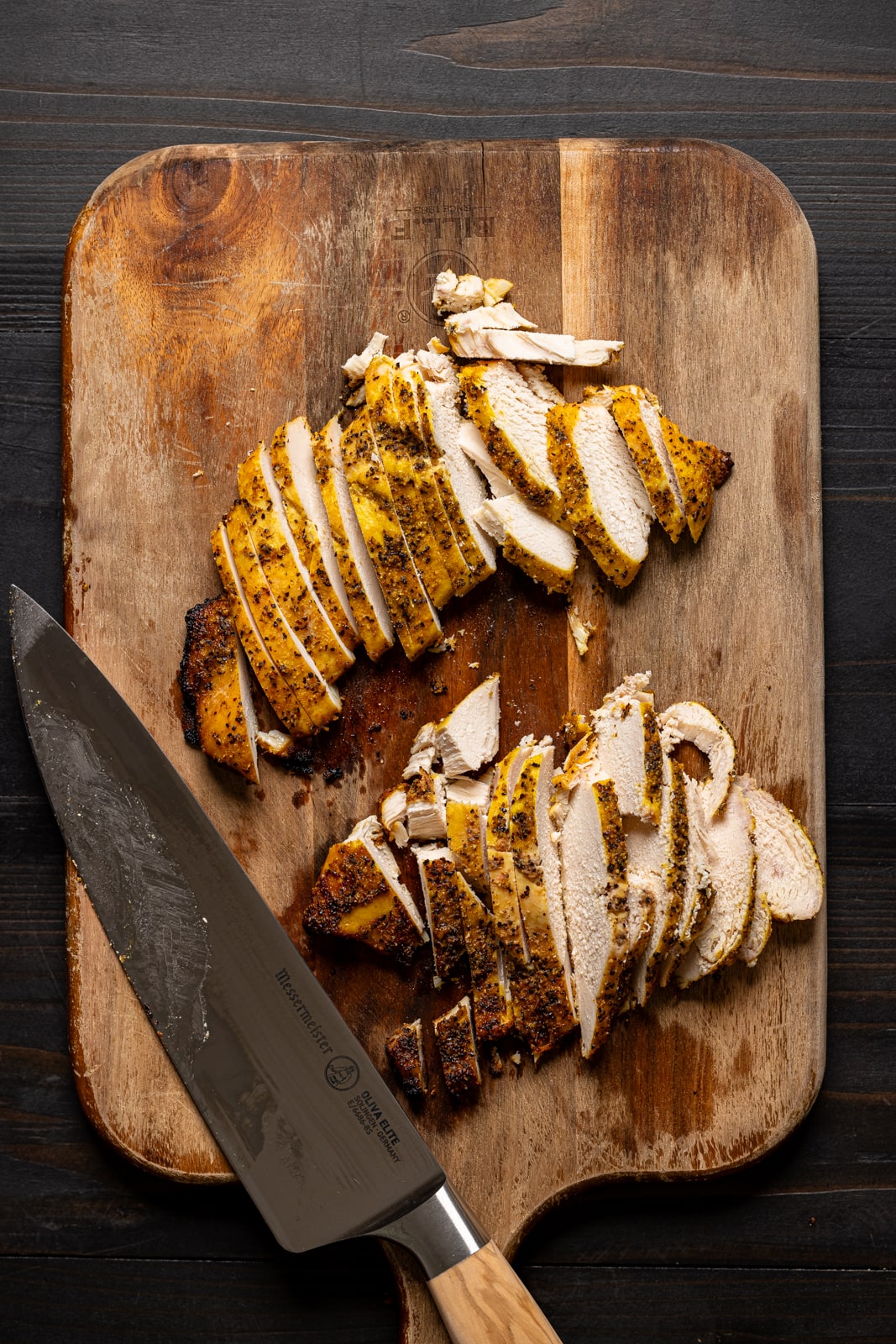 Sliced chicken breasts on a cutting board with a knife.